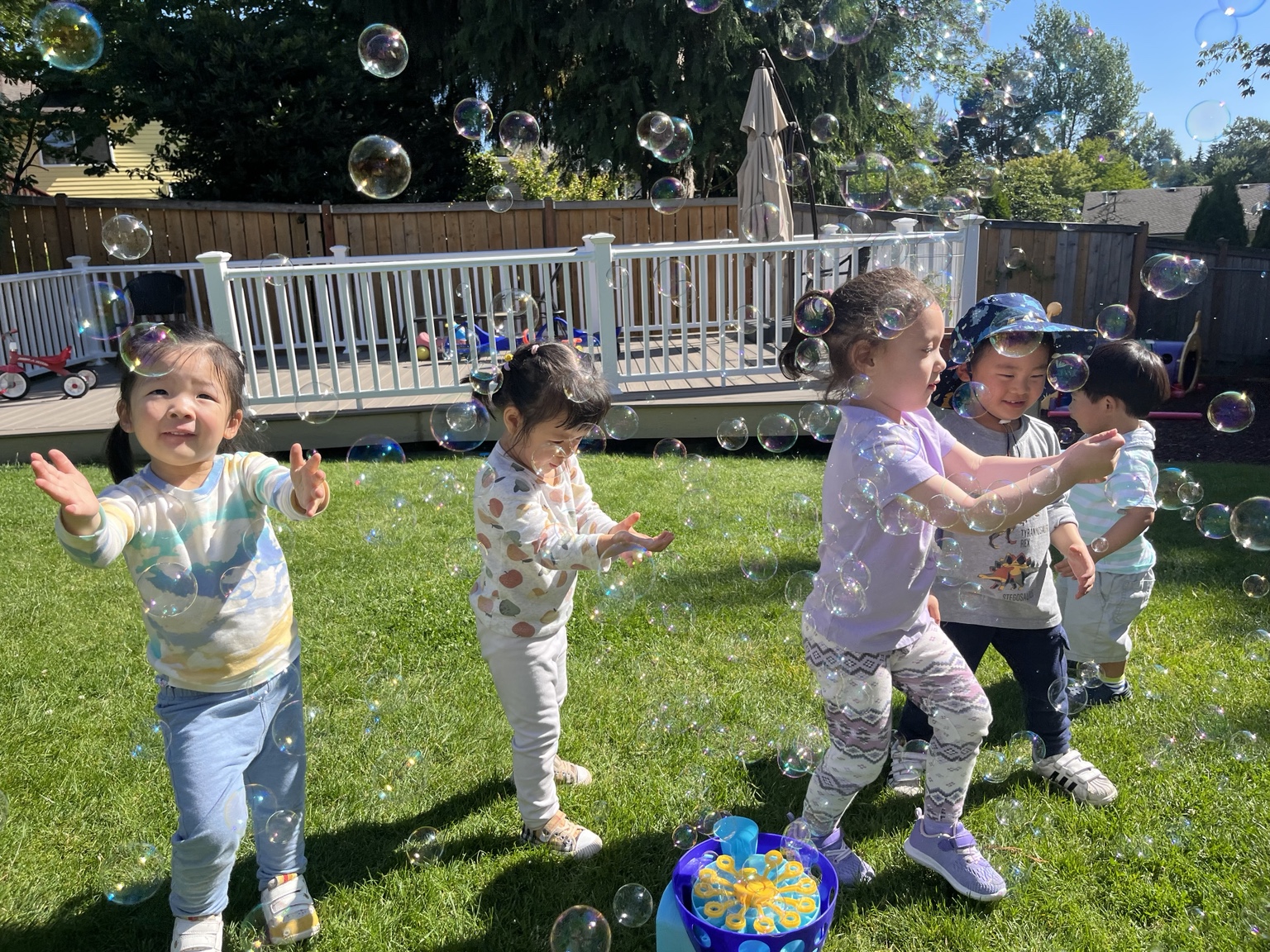Five children playing outdoors in the daycare yard while chasing bubbles